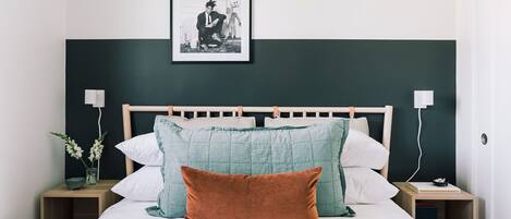 A neatly made bed with a wooden headboard, two bedside tables, and a framed picture on the wall.