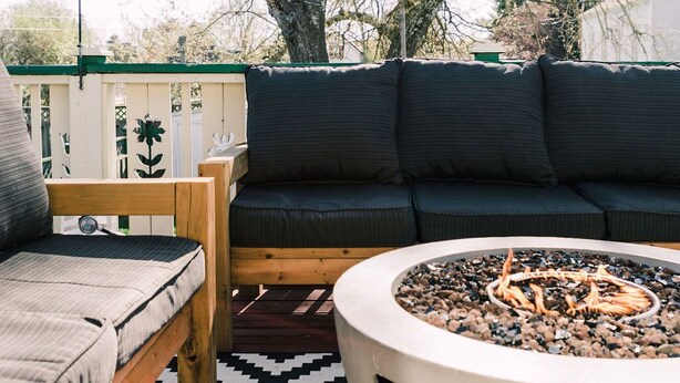Une terrasse dotée d’un foyer rond, d’un banc en bois, d’un canapé et d’une plante suspendue.