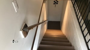 A staircase with a handrail, a light fixture at the top, and a wall-mounted light fixture. - Luxury Apartment in Private Home. Private Entrance. Close to Horse Show, Beaches (Williamsburg)