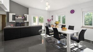 Una cucina moderna con zona pranzo, caratterizzata da un tavolo bianco, sedie nere e un'ampia finestra vista su del verde.