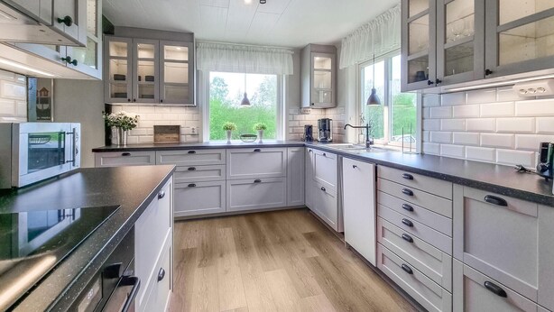 Eine moderne Küche mit weißen Schränken, einem eingebauten Backofen und einem großen Fenster mit Blick ins Freie.
