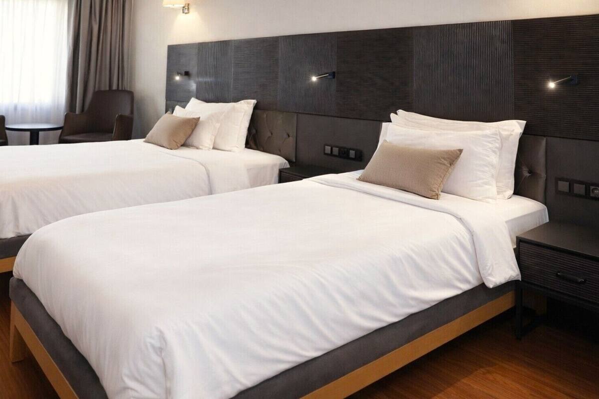 A hotel room with two beds, a dark headboard, and a small table with a chair.