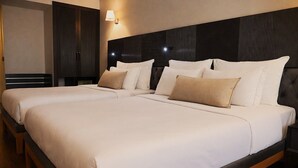 Un lit double avec une literie blanche et beige, une tête de lit sombre et une lampe fixée au mur.