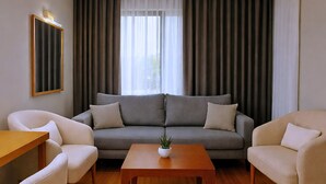 Un salon avec un canapé gris, deux fauteuils beiges, une table basse en bois ornée d’une plante et un tableau encadré accroché au mur.