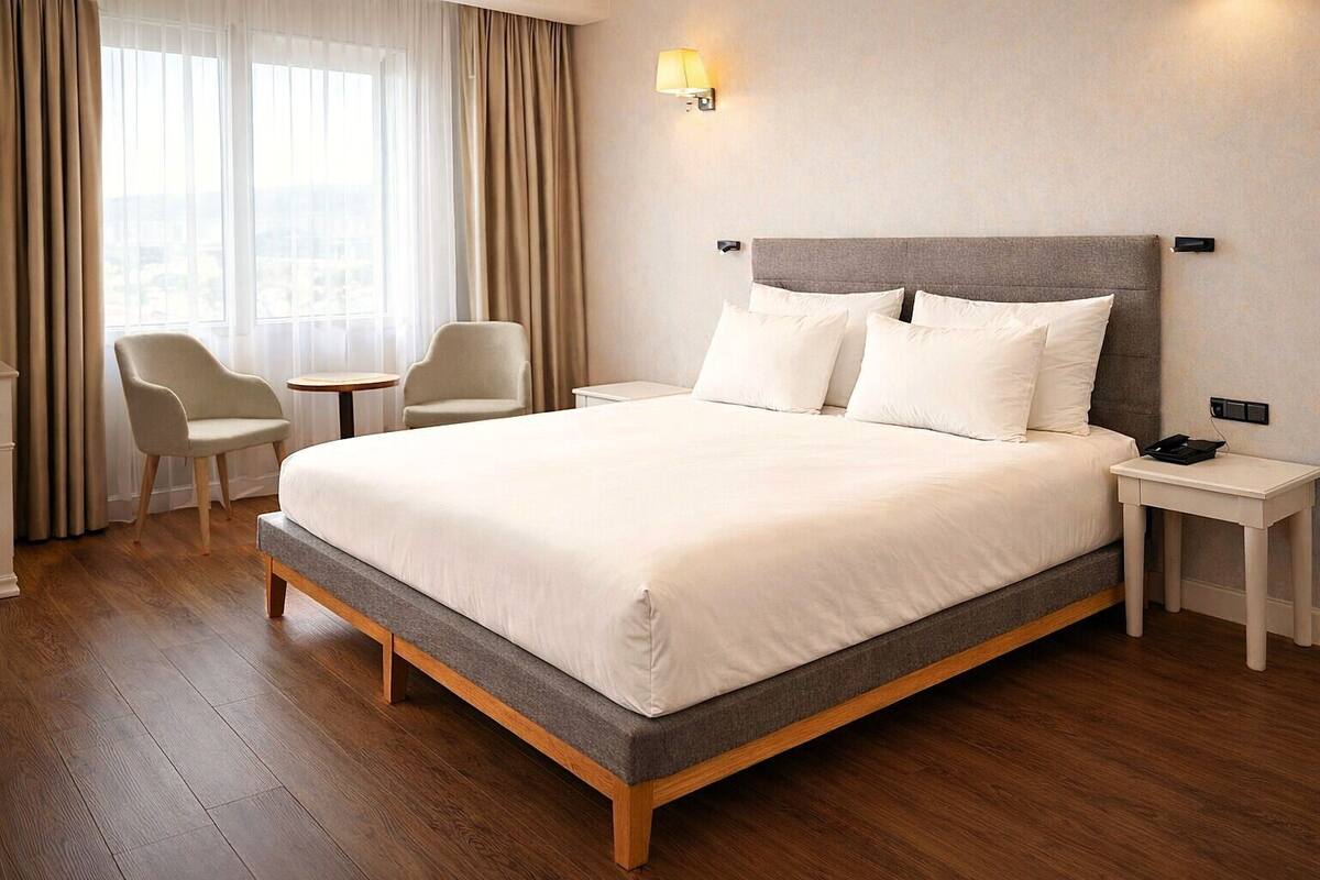 A hotel room with a large bed, two chairs, a small table, and a nightstand with a phone.