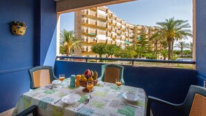 A dining area with a table set for two, a view of a building with balconies, and a palm tree in the background. - Cozy apartment in La Mata, Torrevieja (La Mata, Torrevieja)