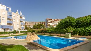 A swimming pool with a rock feature, surrounded by a well-maintained lawn and a multi-story building with balconies. - Cozy apartment in La Mata, Torrevieja (La Mata, Torrevieja)