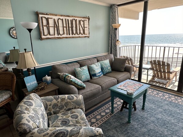 A cozy living room with a sofa, armchairs, and a coffee table. A sign on the wall reads "BEACHHOUSE".