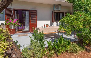 An outdoor seating area with a table and benches, surrounded by various plants and a tree. - Awesome apartment in Raslina (Raslina)