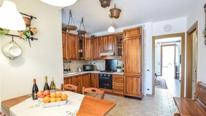 Een keuken met houten kastjes, een eettafel met fruit en wijn, en uitzicht naar buiten.