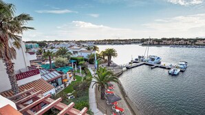 Un port de plaisance avec des bateaux amarrés, un espace piscine avec des parasols, et une vue sur les bâtiments environnants.