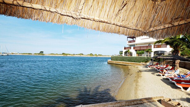 Un hôtel situé en bord de mer, doté d’un toit de chaume, d’un espace de détente au bord de la piscine et offrant une vue sur la mer.