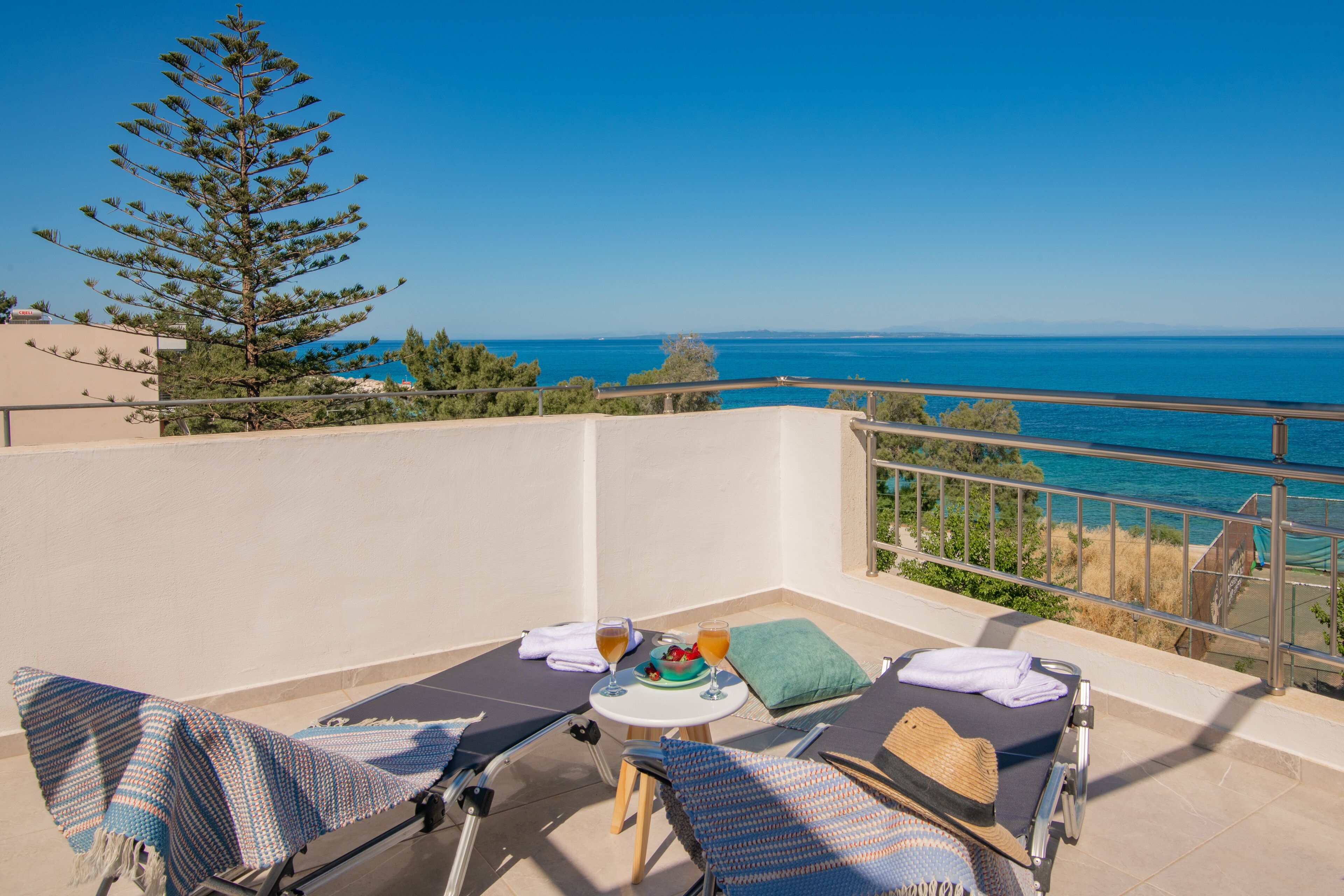 A balcony with two lounge chairs, a small table with a drink and a fruit bowl, and a view of the sea.