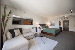 Una habitación de hotel moderna con sofá, una mesita redonda, cama, televisor y espejo.