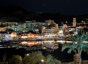 A nighttime view of a coastal town with buildings reflecting on calm water, a prominent tower, and palm trees. - Amazing Views & Pool - Lake Las Vegas Retreat (Henderson)