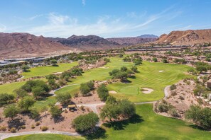 A golf course with a desert landscape, mountains in the background, and a residential area nearby.