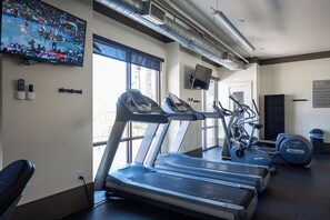 A gym with treadmills, an exercise bike, and a wall-mounted TV displaying a sports event.