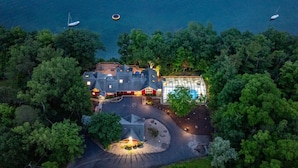 Une vue aérienne d’une maison entourée d’arbres denses, avec une piscine et un quai pour bateaux visibles au loin.