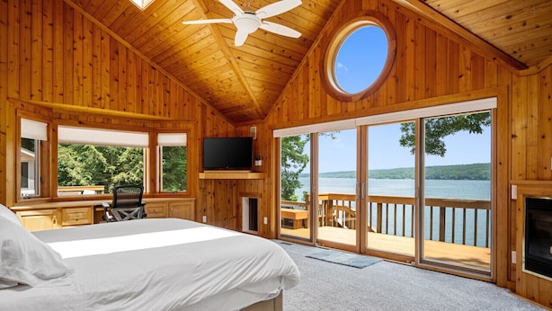Une chambre dans un chalet en bois, avec un lit, une télévision et une grande fenêtre donnant sur un lac.