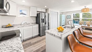 Une cuisine moderne avec des meubles blancs, un réfrigérateur en acier inoxydable, des plans de travail en granit et un coin bar agrémenté de tabourets en cuir.