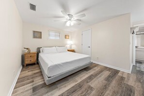 Un dormitorio con una cama, mesitas de noche de madera, un ventilador de techo y una puerta.