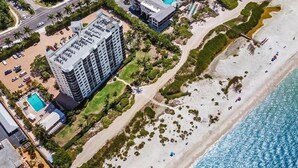 An aerial view of a coastal hotel with a large building, a beach, and a pool. - Gulf Front Beach Life (Fort Myers Beach)