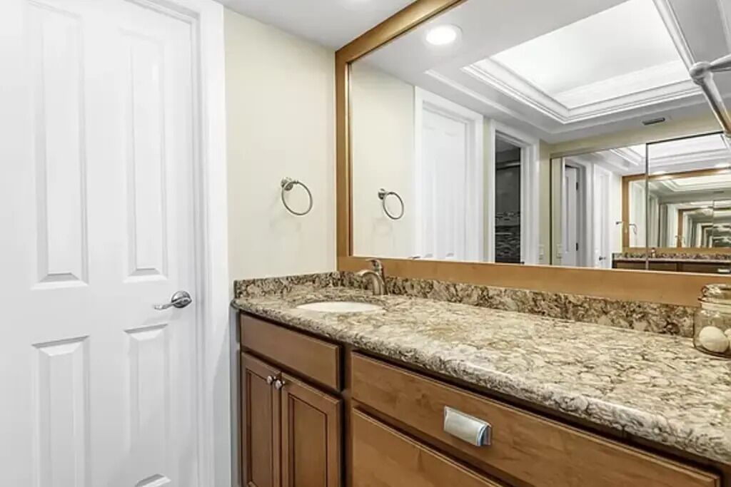 Une salle de bain avec une porte blanche, un grand miroir, un comptoir en granit et un meuble en bois.