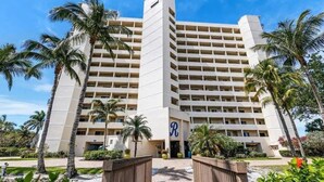 A multi-story hotel with a central entrance, surrounded by palm trees and a clear sky. - Gulf Front Beach Life (Fort Myers Beach)