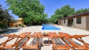 Un espace piscine avec des chaises longues, une structure de jeux en bois et un bâtiment doté d’un toit rouge.