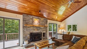 Un salon chaleureux avec une cheminée en pierre, un plafond en bois et une grande fenêtre donnant sur une terrasse.