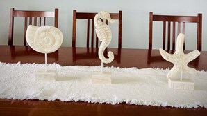 Zona pranzo con uno specchio rotondo, decorazioni a tema pesci e tre sculture a forma di cavalluccio marino su un tavolo.
