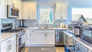 Una cucina moderna con mobili bianchi, forno a microonde integrato, piano cottura, lavastoviglie e macchina da caffè.