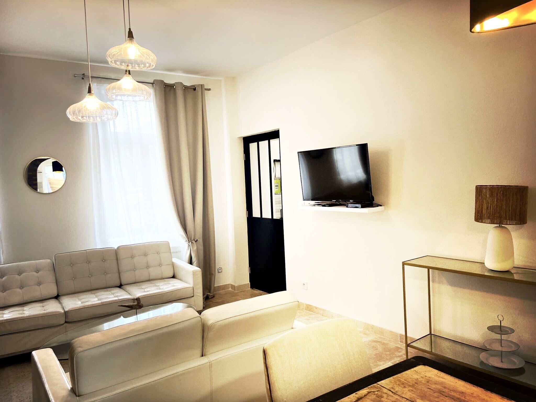 Een moderne woonkamer met een witte bank, een flatscreen televisie aan de muur en een glazen salontafel.