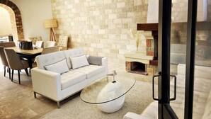 A modern living room with a white sofa, a glass coffee table, and a brick fireplace.