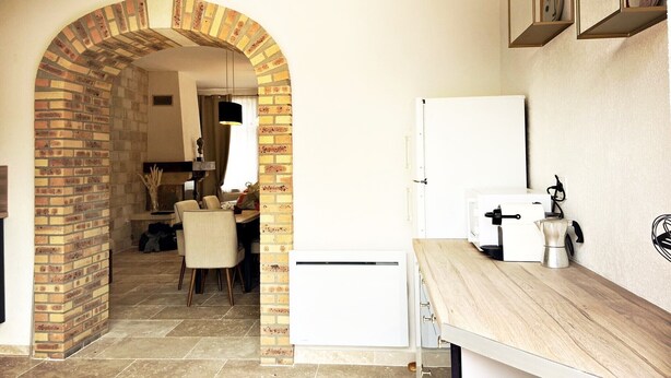 A kitchen with a brick archway leading to a dining area, a white refrigerator, and a wooden countertop with a coffee machine.