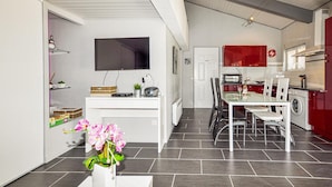 Une cuisine moderne avec un mur de crédence rouge, un coin repas doté d’une table en verre et un téléviseur fixé au mur.