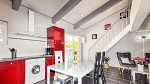Une cuisine moderne avec des meubles rouges, un lave-linge et un coin repas comprenant une table et des chaises en verre.