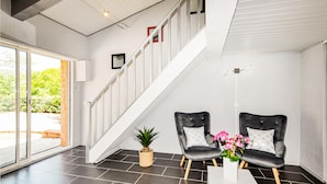 Un intérieur moderne avec un escalier, deux fauteuils en cuir avec des coussins, une table blanche et une plante en pot.