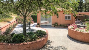 Un chemin de jardin mène à un bâtiment doté d’une entrée fermée par un portail, le tout étant entouré de parterres de fleurs aménagés et d’un petit espace patio.