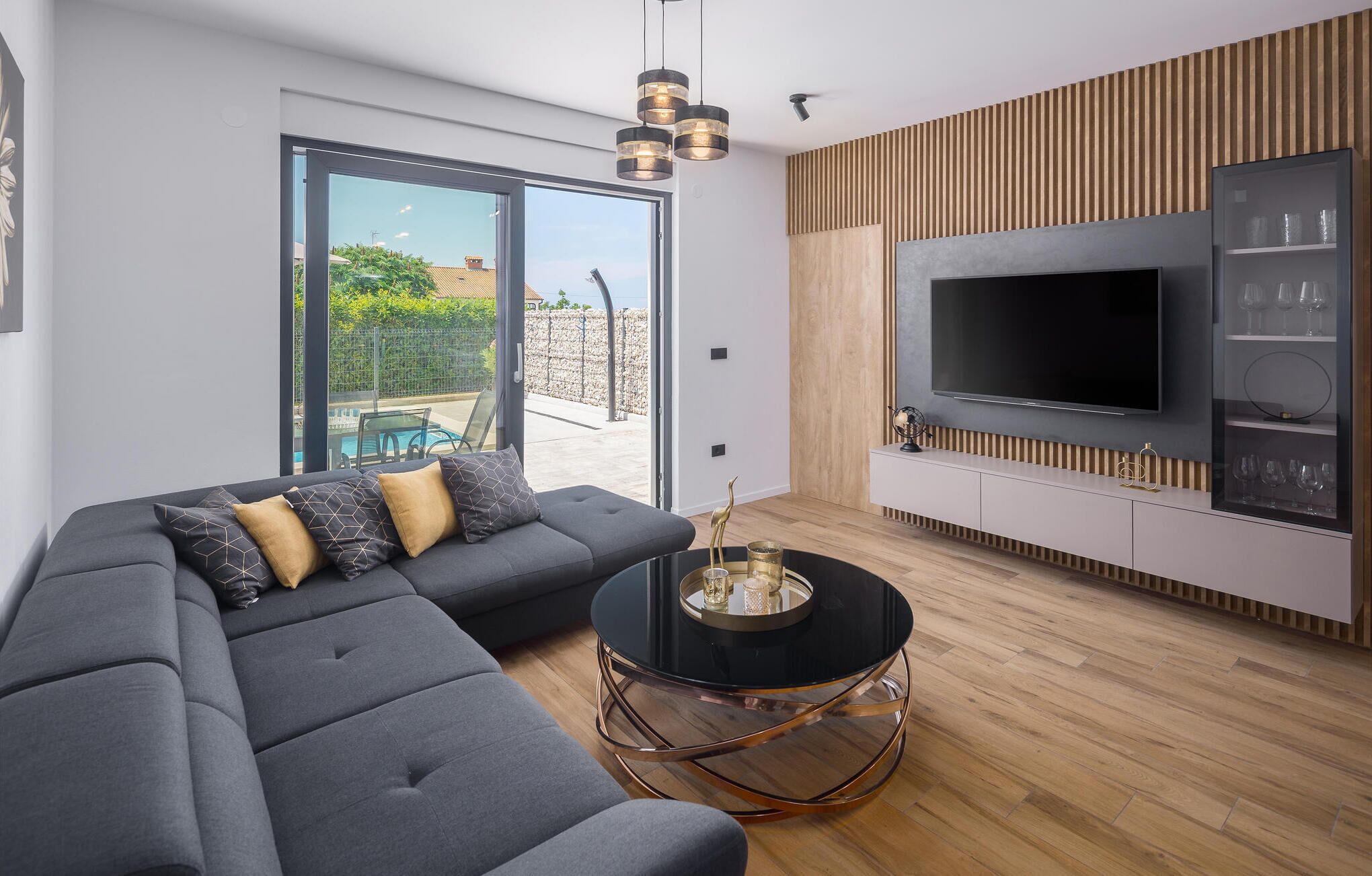Een moderne woonkamer met een modulaire bank, een ronde salontafel en een flatscreen televisie bevestigd aan een houten wandpaneel.