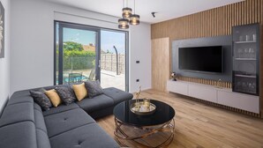 A modern living room with a sectional sofa, a round coffee table, and a flat-screen TV mounted on a wooden panel wall. - Stunning apartment in Radmani (Radmani)