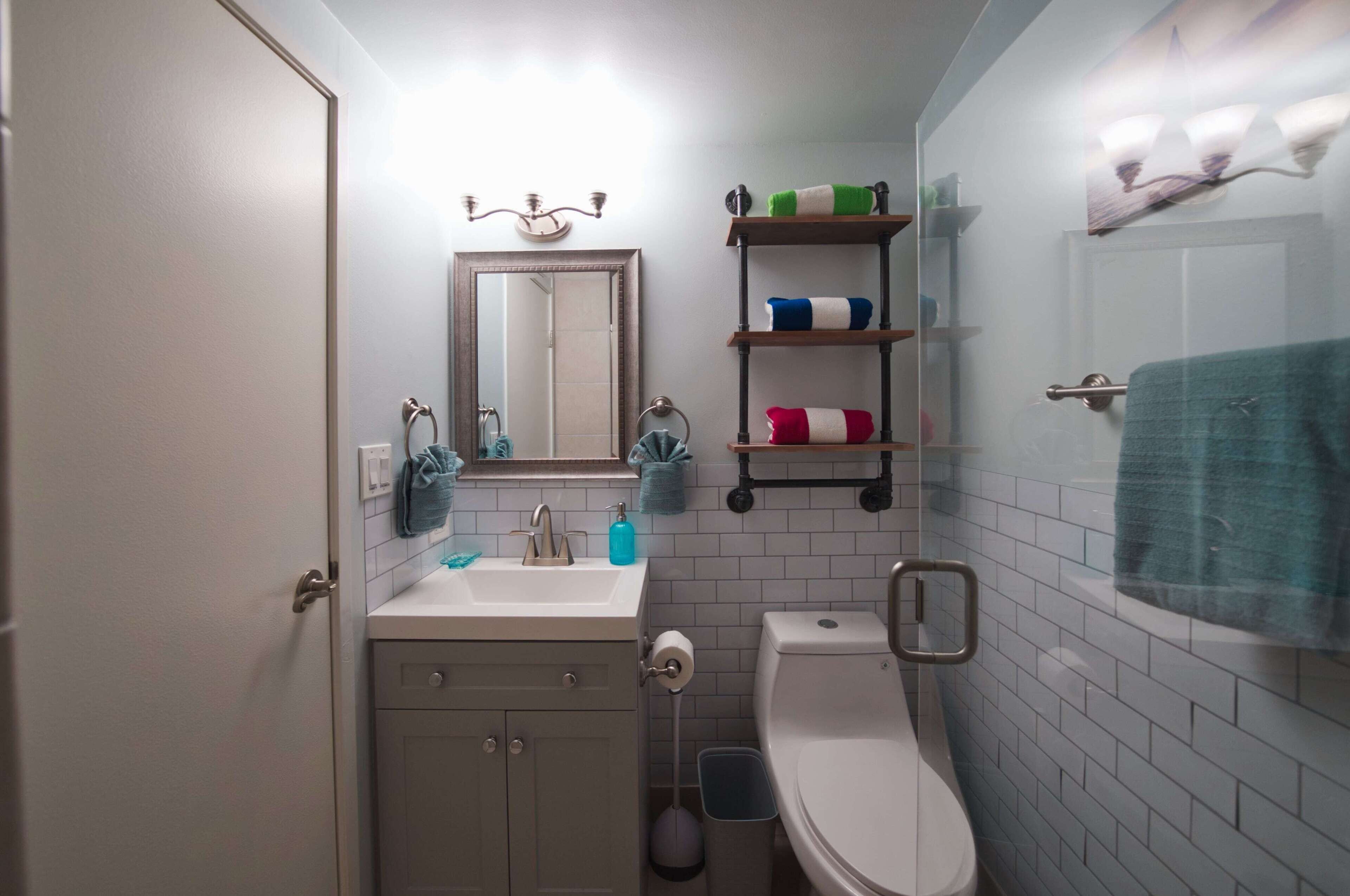 A compact bathroom with a toilet, sink, and mirror. There are shelves with towels and toiletries.