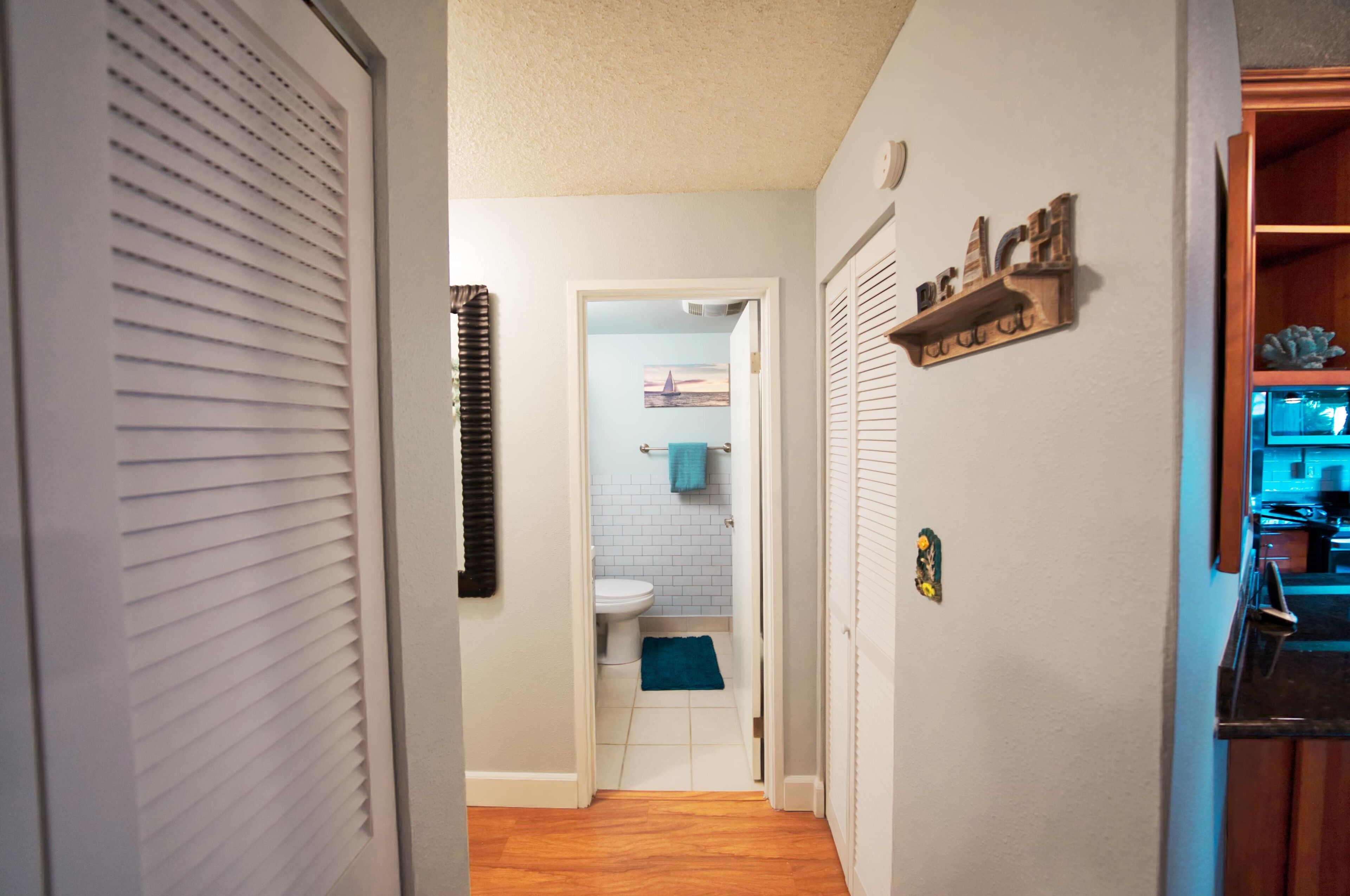 A narrow hallway leading to a bathroom with a toilet and a blue towel on the floor.