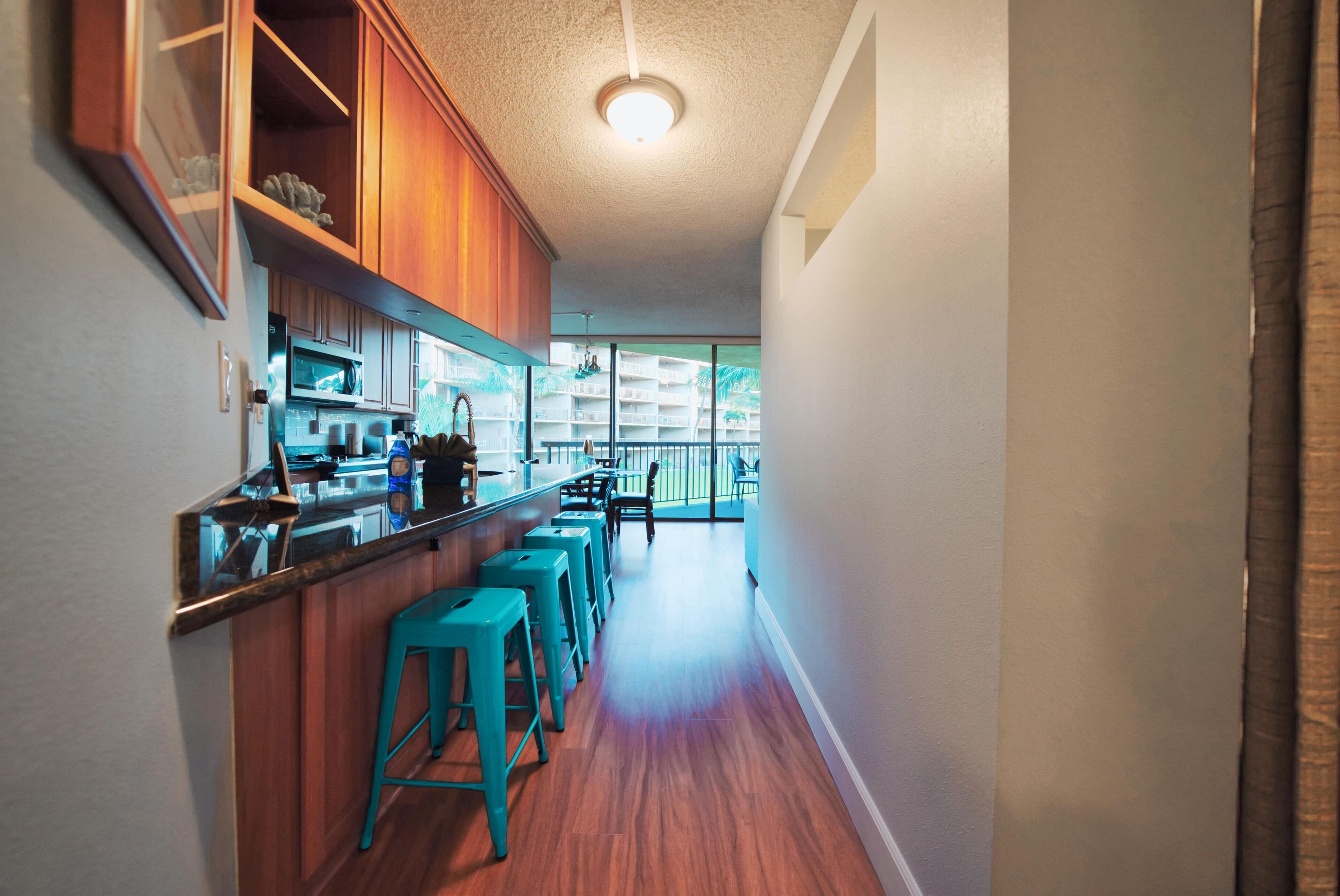 A kitchen with wooden cabinets, a bar area with stools, and a view of a balcony.