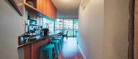 A kitchen with wooden cabinets, a bar area with stools, and a view of a balcony.