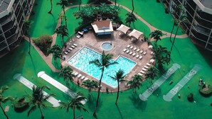 An aerial view of a hotel with a central swimming pool surrounded by lounge areas, palm trees, and a tennis court. - Spacious Maui Sunset Condo: Steps to BEACH. Pool, Gym, AC & Family Friendly (Kihei)