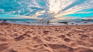 A beach with a sandy foreground and a view of the ocean under a cloudy sky. - Spacious Maui Sunset Condo: Steps to BEACH. Pool, Gym, AC & Family Friendly (Kihei)