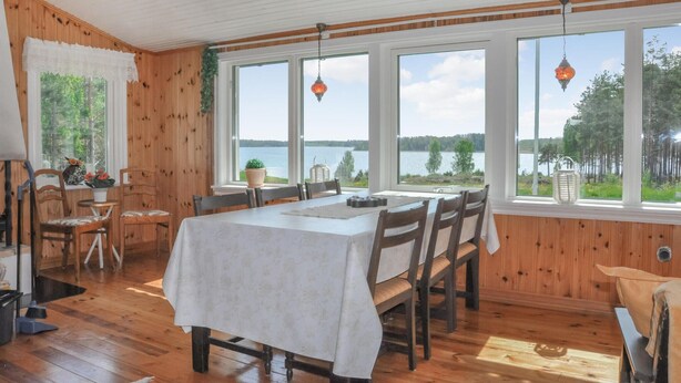Uma sala de jantar com mesa posta para seis, grandes janelas com vista para um lago, paredes de madeira e lanternas penduradas.