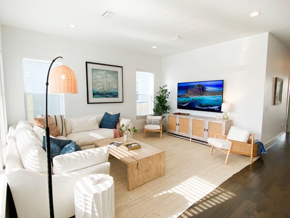 A modern living room with a white sofa, a coffee table, a TV, and a large window.