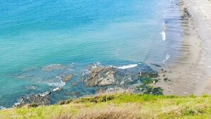 Eine Küstenlandschaft mit Strand, klarem blauen Meer, Felsen und einem Gebäude mit einem Balkon mit Meerblick.